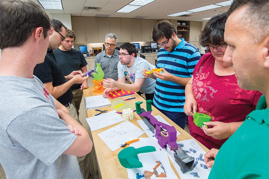 Professor Tommy James (second from left) leads his Intro to 3-D Printing class in examining and critiquing each other’s latest prototypes.