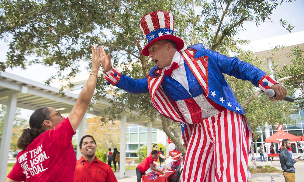 Student Development program specialist and 2016 Distinguished Graduate Emmy Torres goes up top for a high five with the stiltswalker at the West Campus Veterans Day event, Nov. 9, 2017.